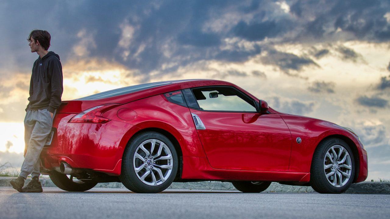 Man leaning on a red sports car at sunset.